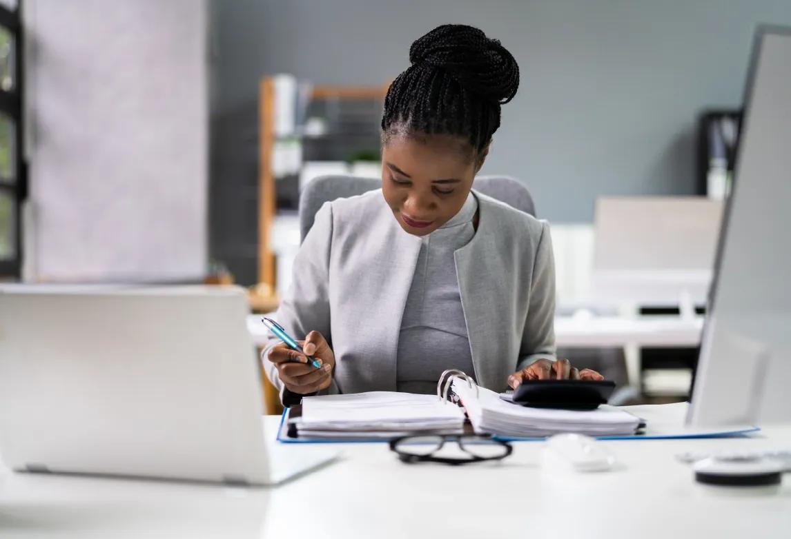 accounting professional holding a calculator above a binder of financial information