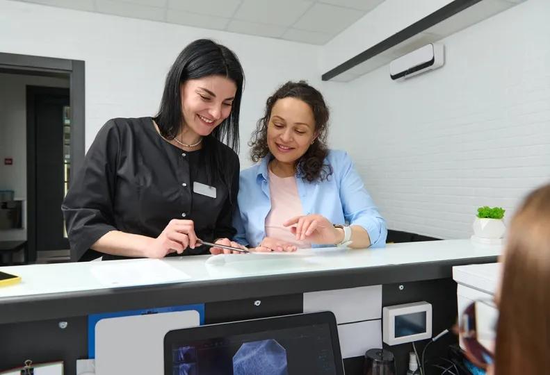 a medical administrative assistant and medical assistant standing by the front desk of a healthcare office