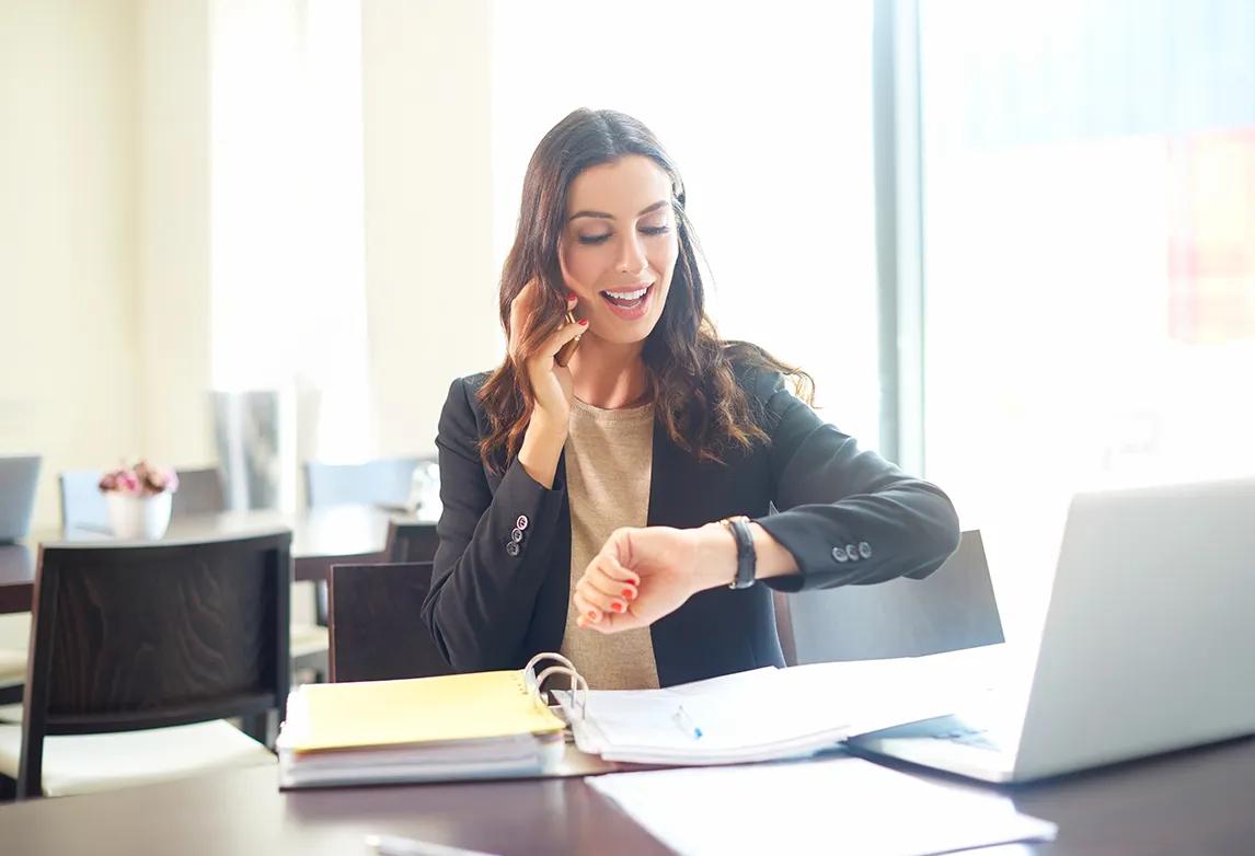 Healthcare professional talking on the phone and looking at her watch as a time management technique