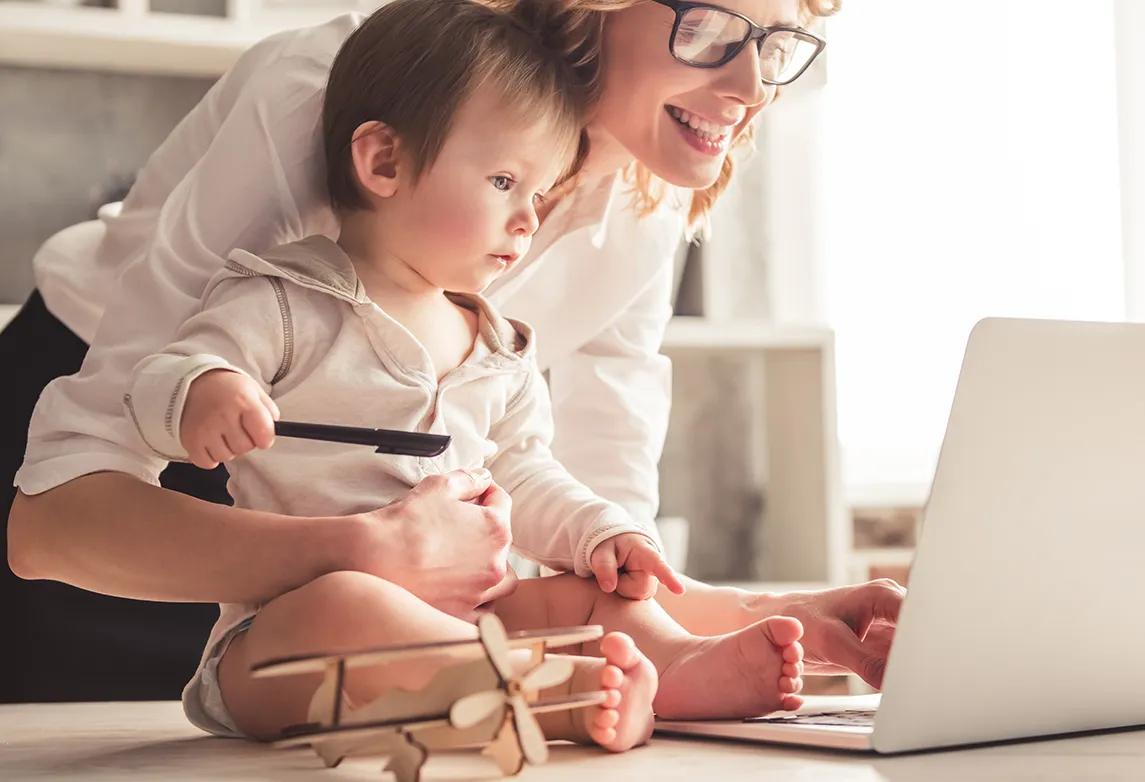 A woman works on her computer while watching her child to signify positive time management skills.