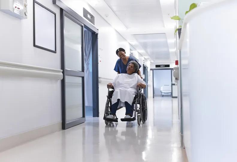 a healthcare professional pushing a patient in a wheelchair and smiling because she is in a job that helps people